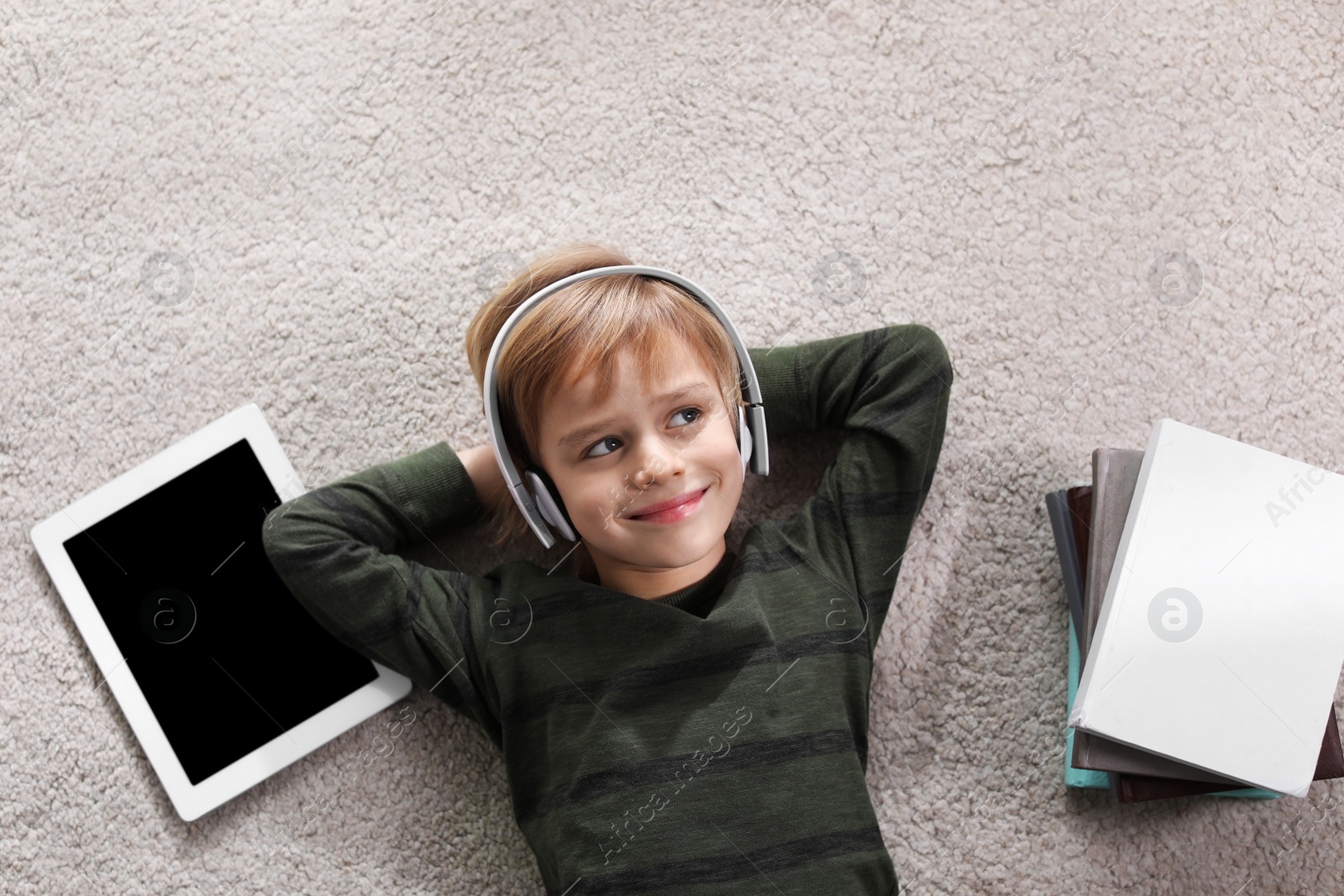 Photo of Cute little boy with headphones and tablet listening to audiobook on floor indoors, flat lay