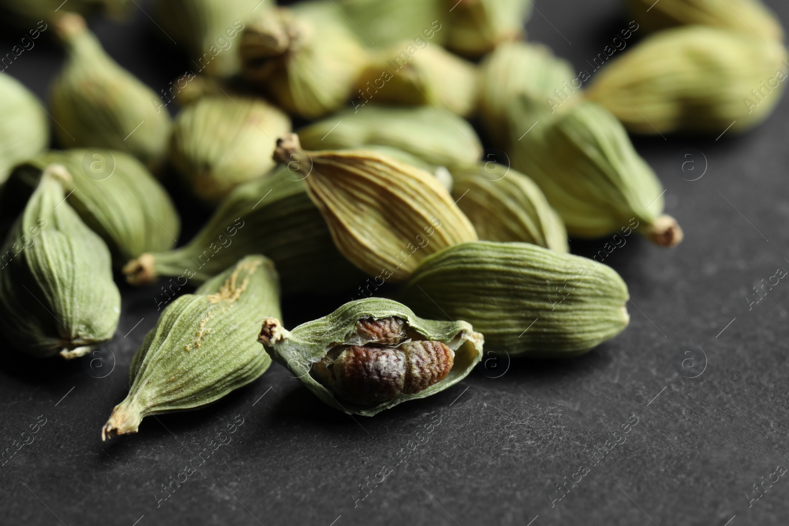 Photo of Pile of dry cardamom pods on black table, closeup