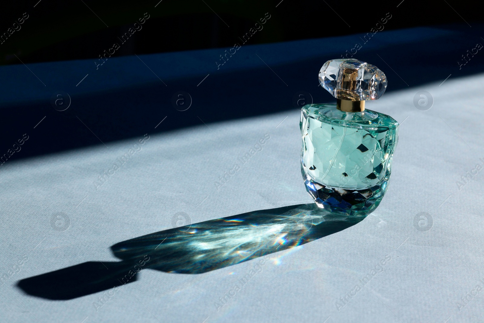 Photo of Luxury women's perfume. Sunlit glass bottle on grey background. Space for text