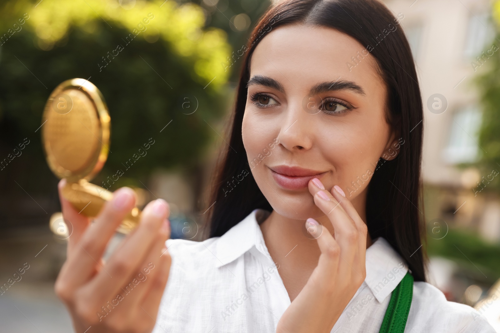 Photo of Beautiful young woman looking at herself in cosmetic pocket mirror outdoors