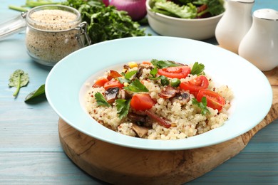 Photo of Plate of tasty quinoa porridge with fried bacon, mushrooms and vegetables on light blue wooden table, closeup