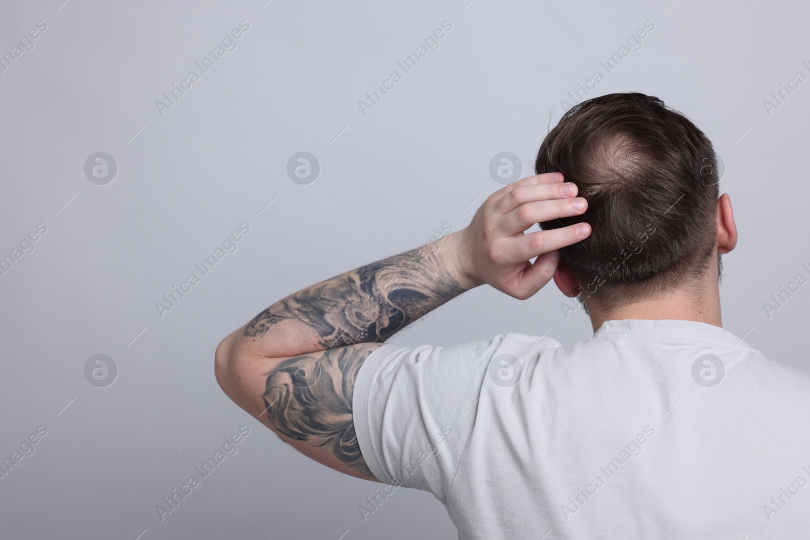 Photo of Baldness concept. Man with bald spot on light grey background, back view. Space for text