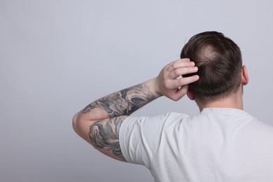 Baldness concept. Man with bald spot on light grey background, back view. Space for text