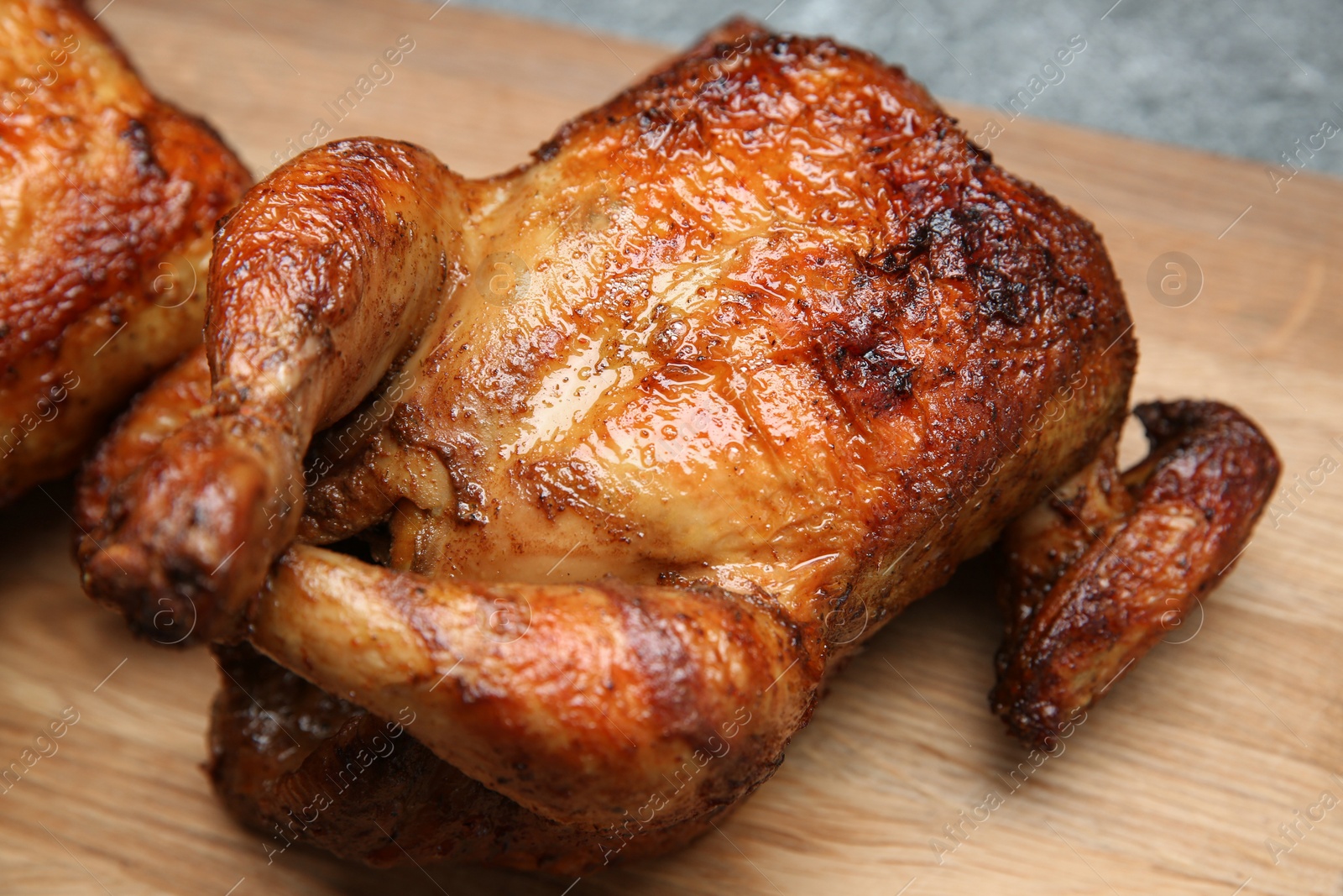 Photo of Delicious grilled whole chicken on wooden board, closeup