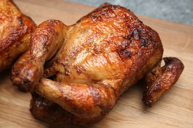 Photo of Delicious grilled whole chicken on wooden board, closeup