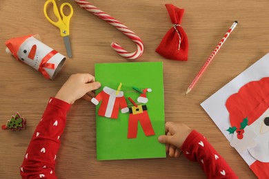 Little child with beautiful Christmas greeting card at wooden table, top view