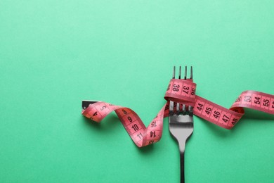 Fork with measuring tape on green background, top view with space for text. Diet concept