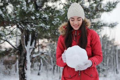 Young woman holding snowball outdoors on winter day. Space for text