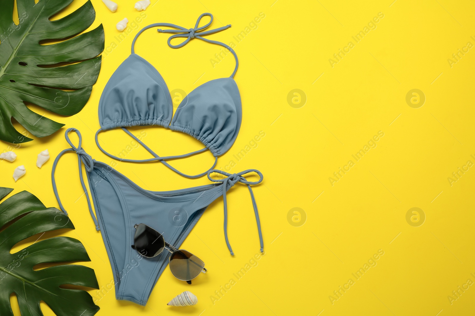 Photo of Stylish blue bikini, sunglasses and leaves on yellow background, flat lay. Space for text