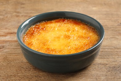 Photo of Delicious creme brulee in ceramic ramekin on wooden table, closeup