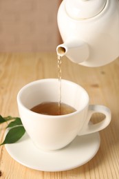 Pouring tasty tea into cup at light wooden table, closeup