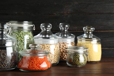 Photo of Different types of legumes and cereals in glass jars on wooden table. Organic grains