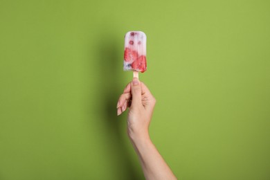 Photo of Woman holding berry popsicle on green background, closeup