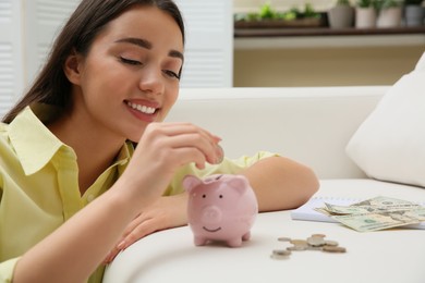 Photo of Woman putting coin into piggy bank indoors. Money savings
