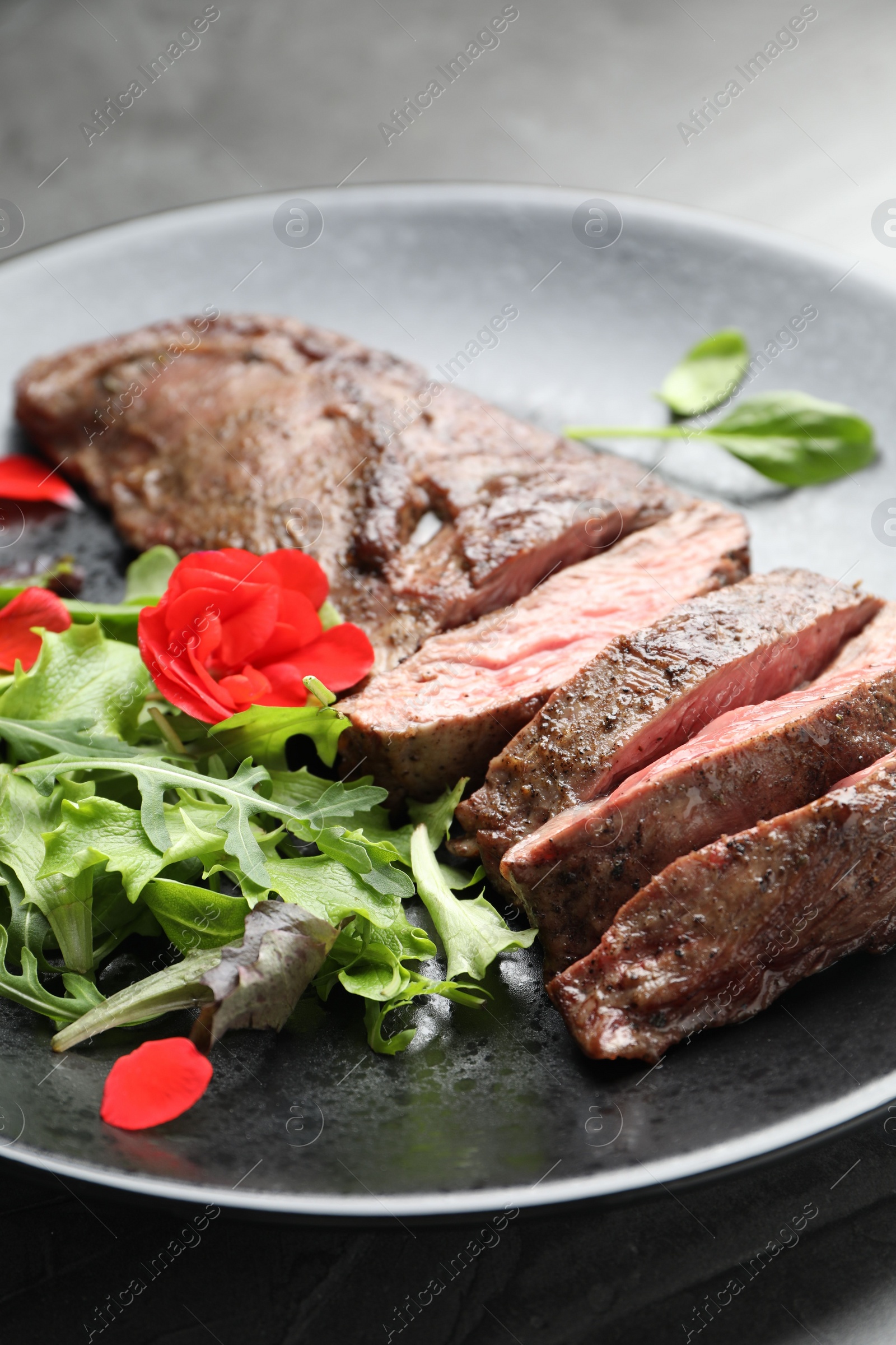 Photo of Pieces of delicious grilled beef meat and greens on table, closeup