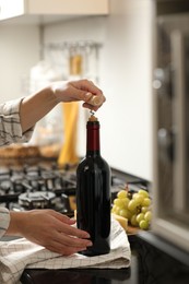 Photo of Woman opening wine bottle with corkscrew at countertop indoors, closeup