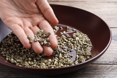 Woman with gold nuggets at wooden table, closeup