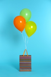 Paper bag with bright air balloons on color background