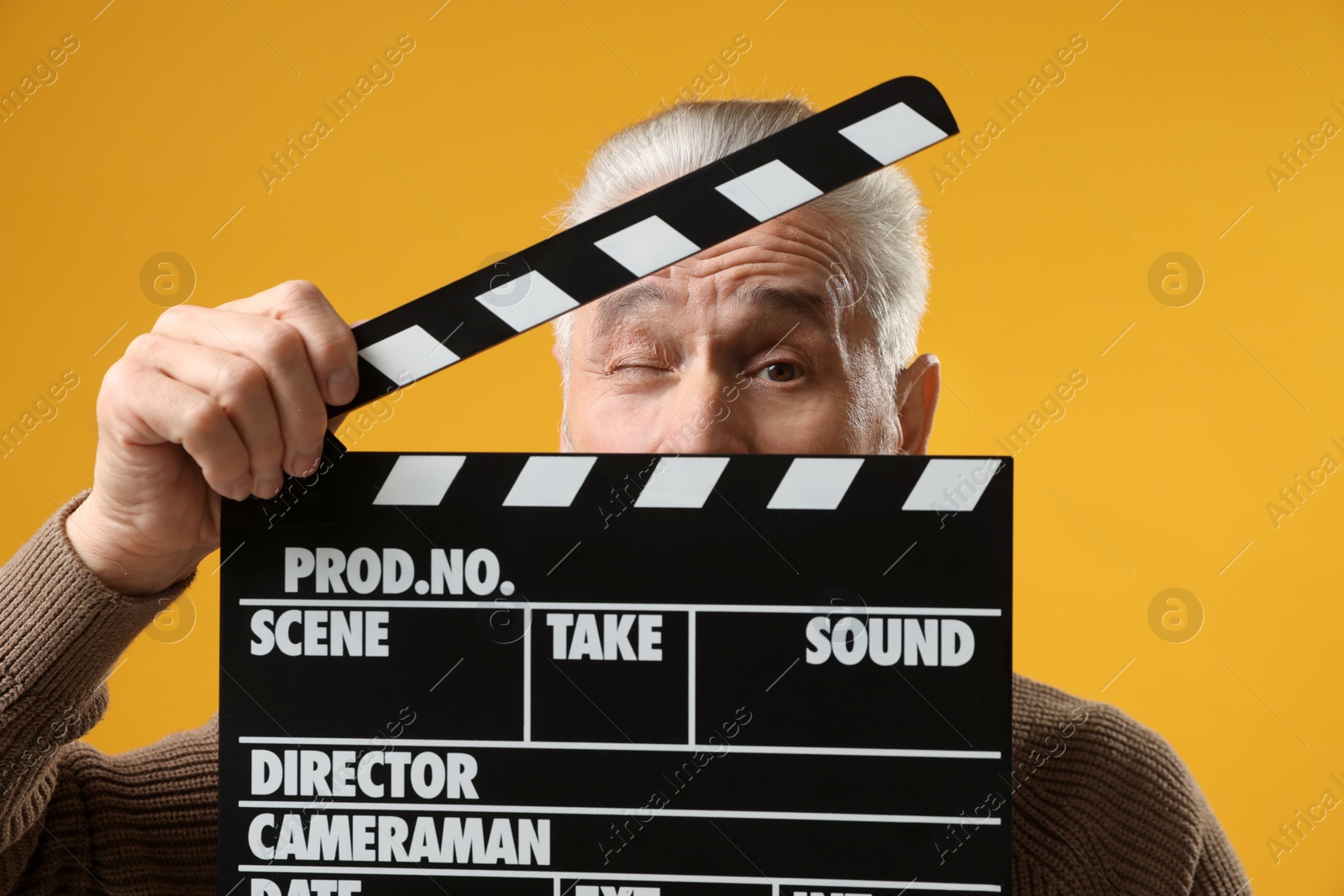 Photo of Senior actor holding clapperboard on yellow background. Film industry