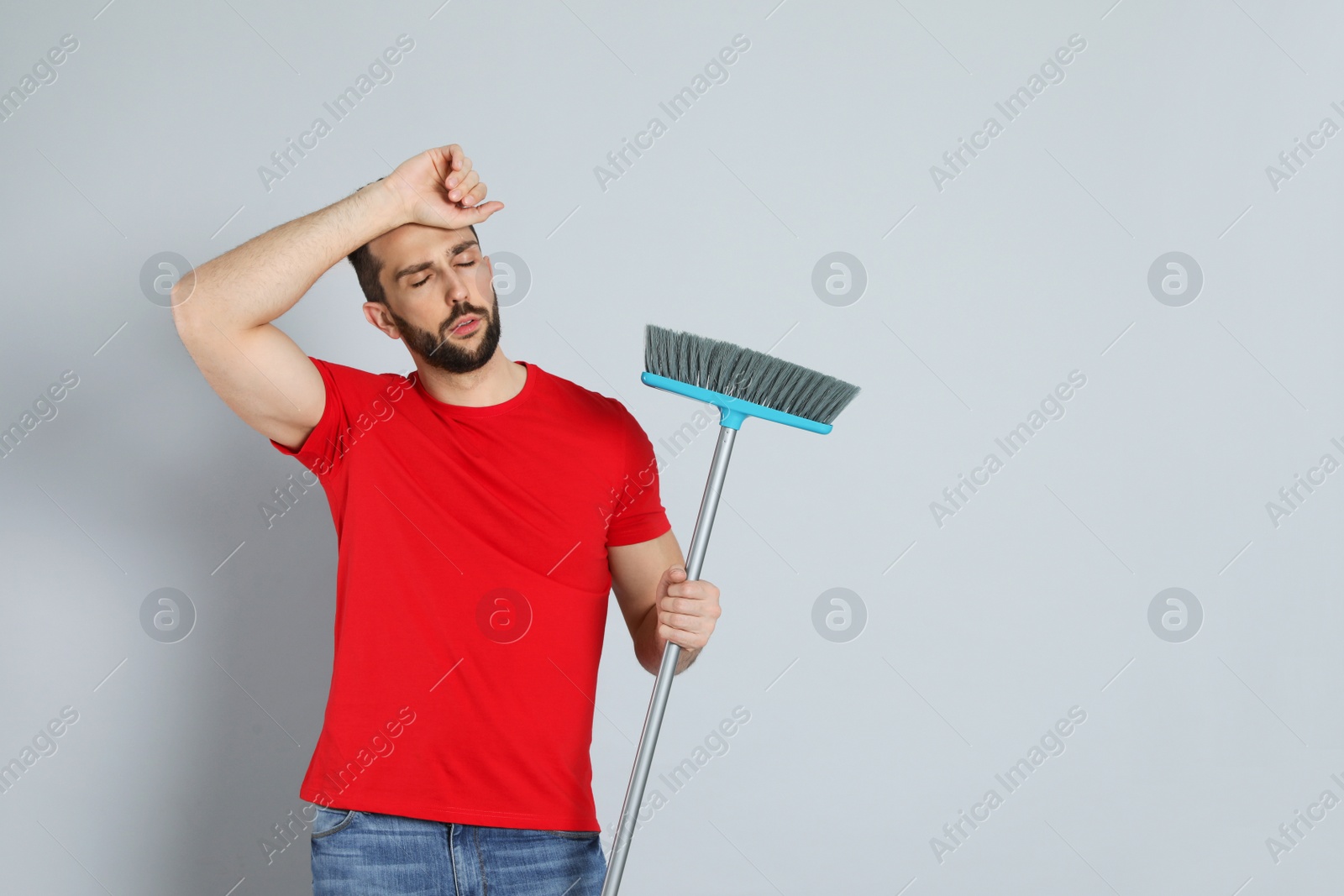 Photo of Tired man with broom on grey background, space for text