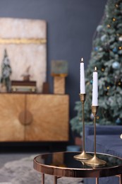 Pair of beautiful candlesticks on glass table and Christmas decor in room, space for text