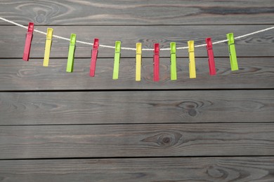 Photo of Colorful plastic clothespins on rope against wooden background. Space for text