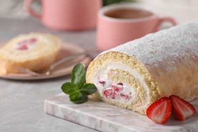 Delicious sponge cake roll with strawberries and cream on light grey table, space for text