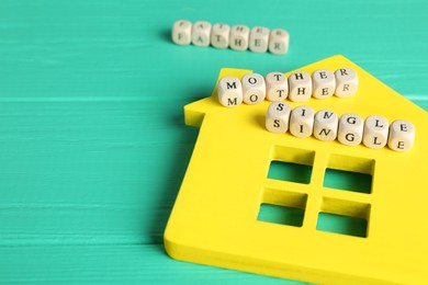 Photo of House model and cubes with text Single Mother on turquoise wooden table, closeup