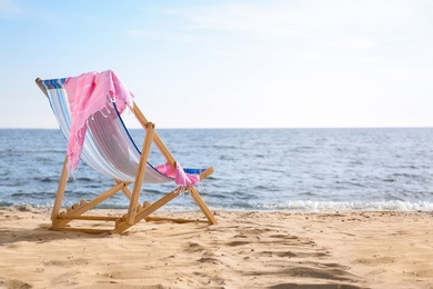 Lounger and towel on sand near sea, space for text. Beach objects
