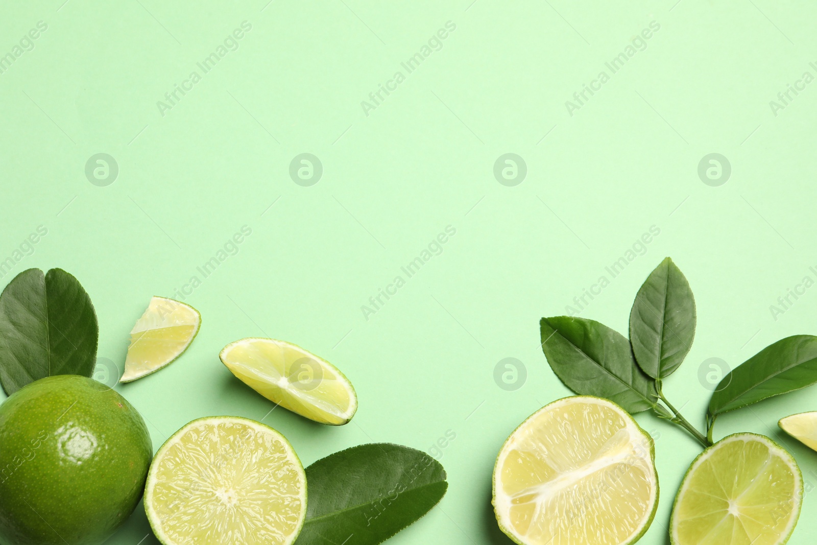 Photo of Whole and cut fresh ripe limes with leaves on light green background, flat lay