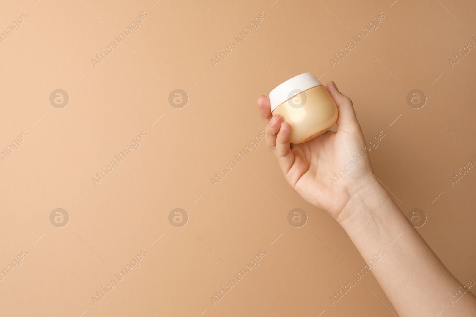 Photo of Woman holding jar of face cream on beige background, closeup. Space for text