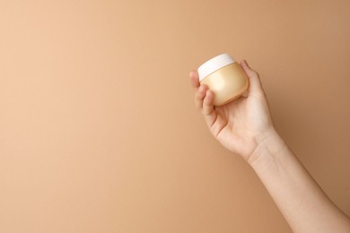 Woman holding jar of face cream on beige background, closeup. Space for text