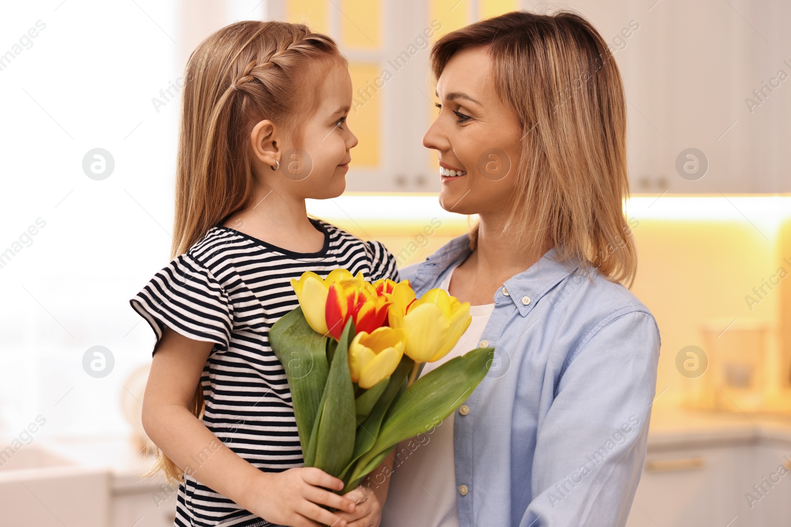 Photo of Little daughter congratulating her mom with bouquet of beautiful tulips at home. Happy Mother's Day