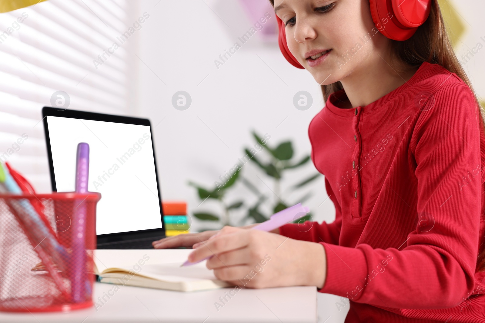 Photo of E-learning. Girl taking notes during online lesson at table indoors, closeup