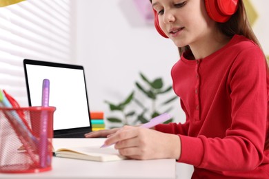 Photo of E-learning. Girl taking notes during online lesson at table indoors, closeup