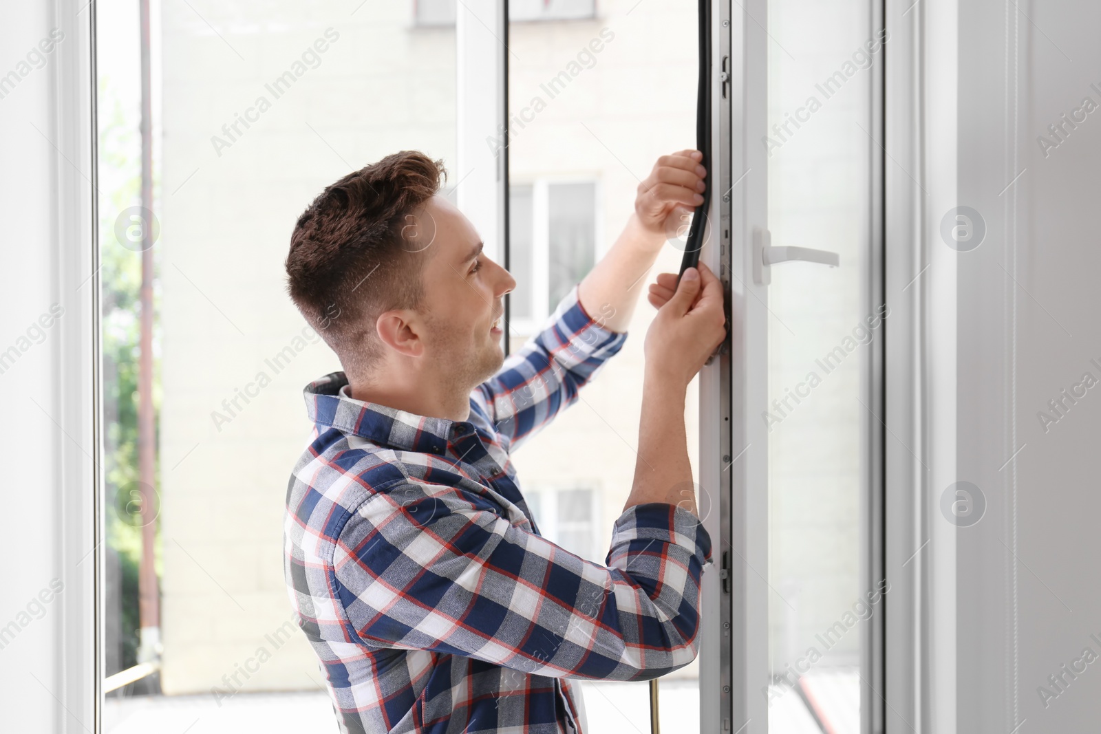 Photo of Young man putting sealing foam tape on window indoors