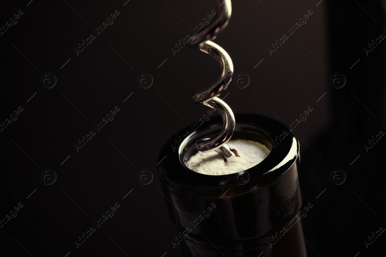 Photo of Opening bottle of wine with corkscrew on dark background, closeup