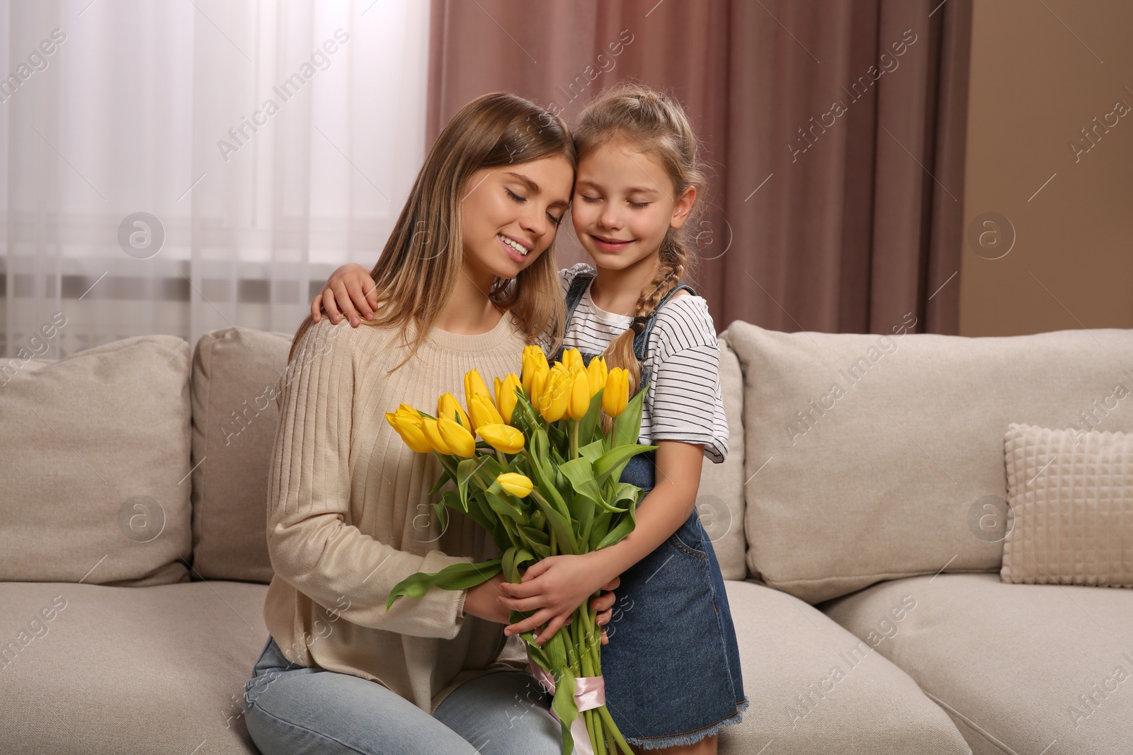 Photo of Little daughter congratulating mom with bouquet of yellow tulips at home. Happy Mother's Day