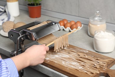 Photo of Woman making soba with pasta machine at table in kitchen, closeup