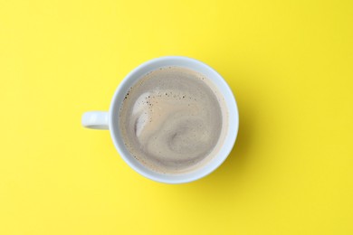 Photo of White mug of freshly brewed hot coffee on yellow background, top view