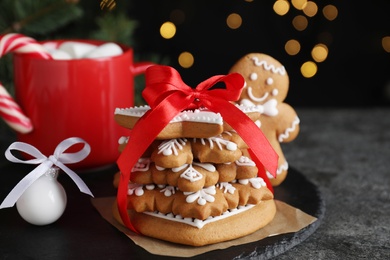 Decorated Christmas cookies and cup of delicious drink on grey table against blurred festive lights