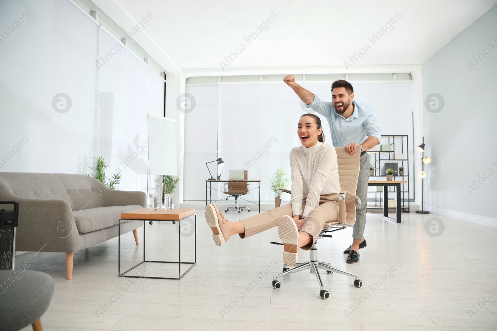 Photo of Office employee giving his colleague ride in chair at workplace. Space for text