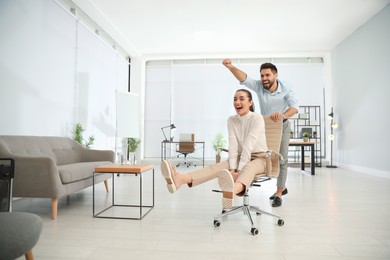 Office employee giving his colleague ride in chair at workplace. Space for text