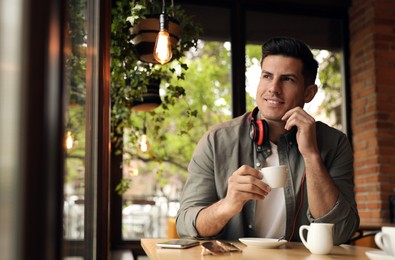 Handsome man with cup of coffee at cafe in morning