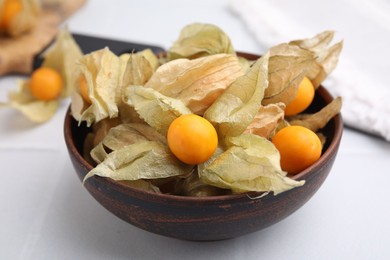 Ripe physalis fruits with calyxes in bowl on white table, closeup