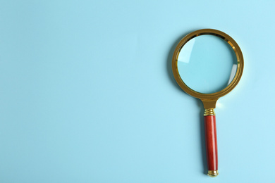 Top view of magnifying glass on light blue background, space for text. Search concept