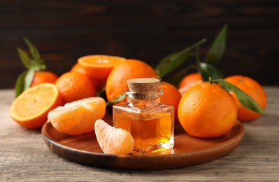 Photo of Bottle of tangerine essential oil and fresh fruits on wooden table