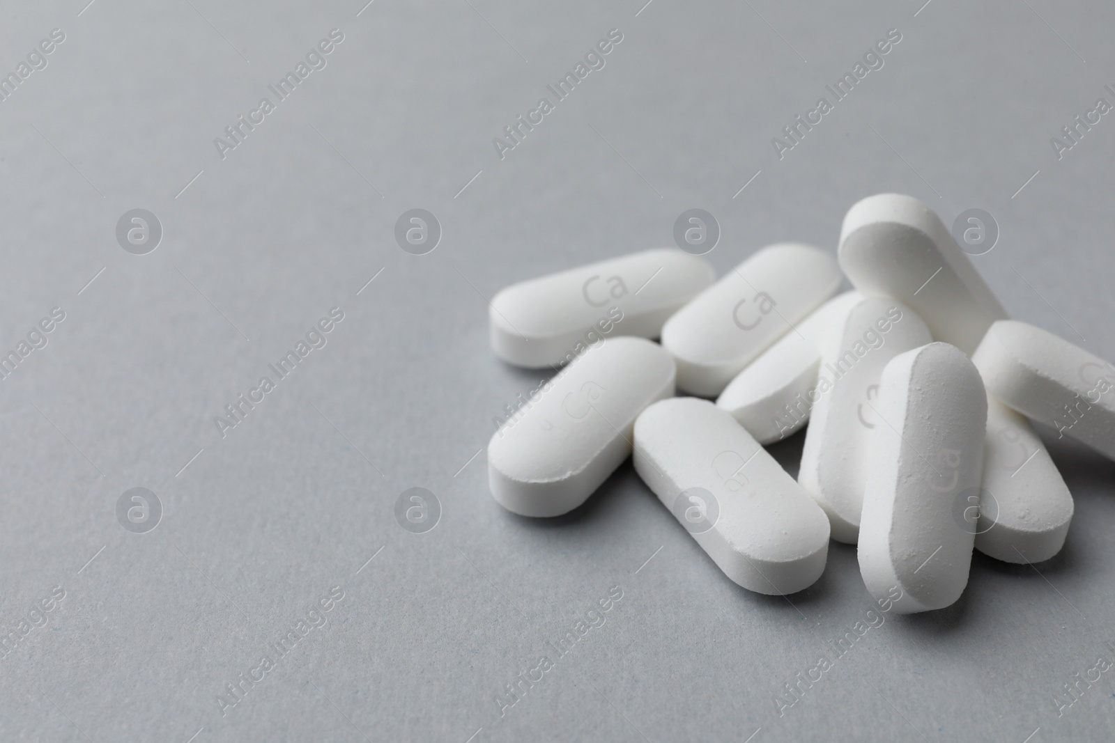 Photo of Pile of calcium supplement pills on light grey background, closeup. Space for text