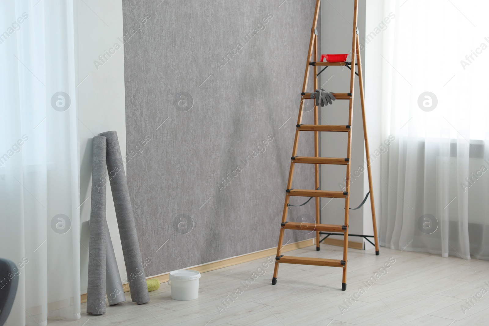 Photo of Wallpaper rolls, bucket with glue and wooden ladder in room