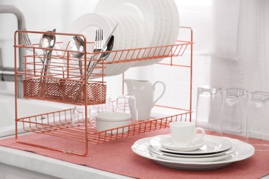 Drying rack with clean dishes and cutlery on countertop in kitchen